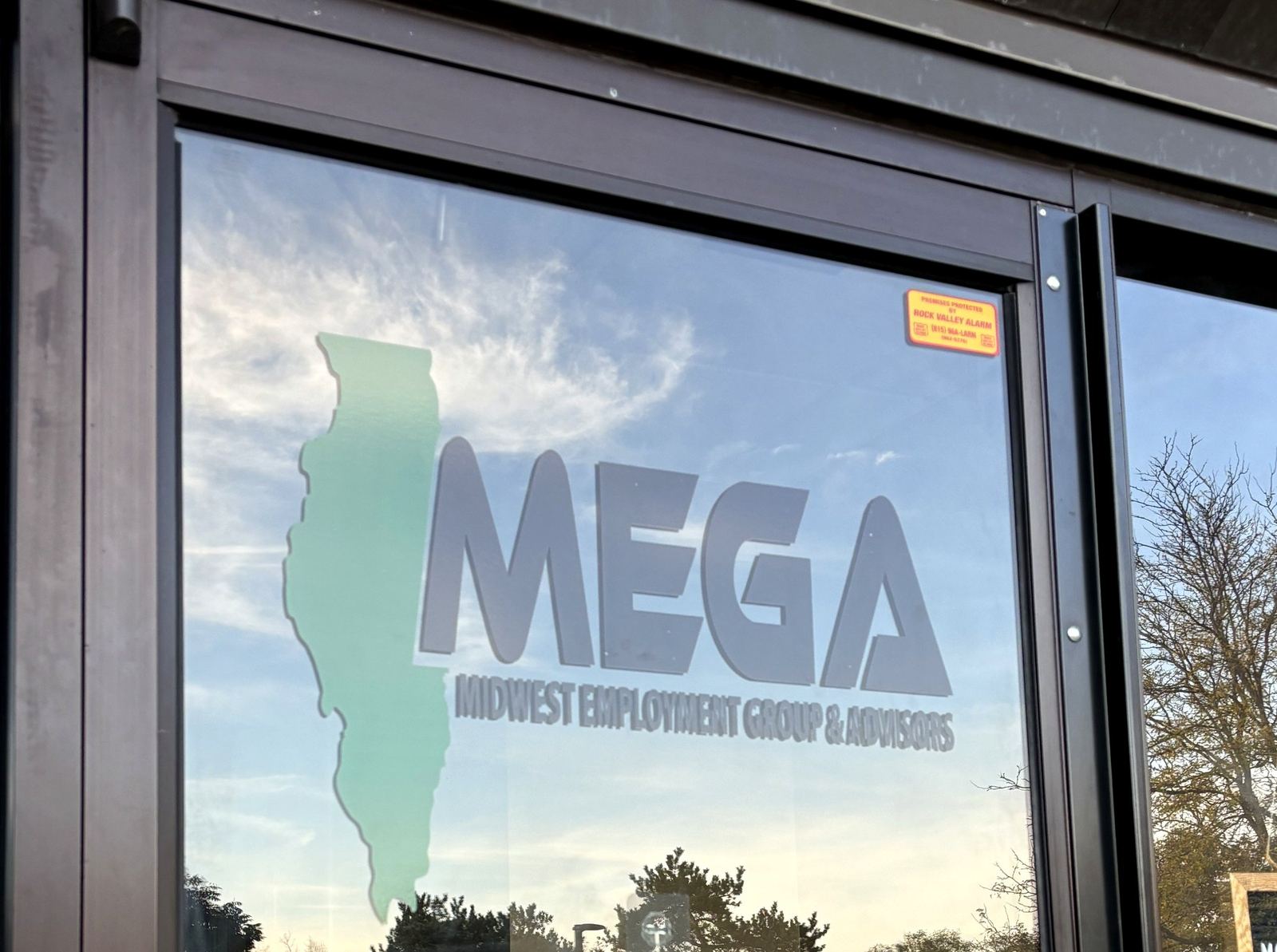 The MEGA front office door in Rockford, Illinois — logo etched on glass with sunset reflection